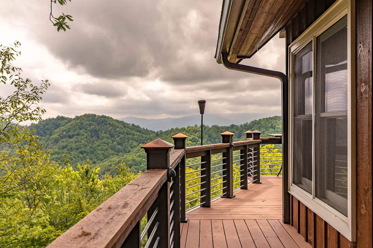A tranquil wooden deck with sturdy railings overlooks an expansive mountainous landscape. The area is perfect for quiet mornings with coffee, peaceful reading, or small gatherings set against breathtaking scenery.