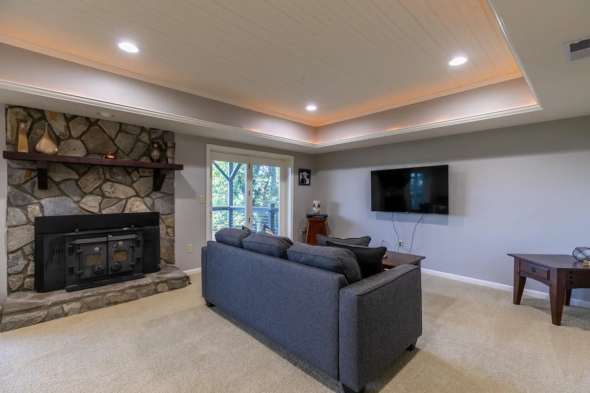 This image features a cozy living area anchored by a striking stone fireplace, a plush sofa, a television, and large windows that bring in natural light. The overall mood is inviting and encourages relaxation, socialization, and shared movie nights, which aligns perfectly with the section's mention of gathering spots and entertainment amenities.