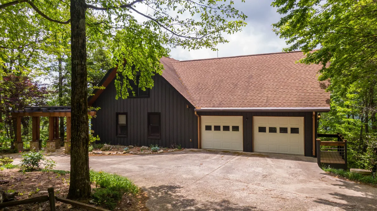 The welcoming exterior of Rockcliff Retreat, showcasing a wooden porch, neatly landscaped garden, and a two-car garage. The porch invites gatherings, while the setting hints at mountain adventures beyond.