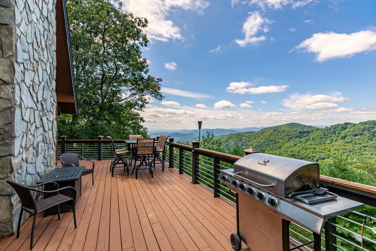 An inviting exterior setup with a grill and outdoor dining set placed on a deck overlooking a stunning mountain view. The space is ideal for al fresco dining, barbecuing, or simply soaking in the scenery, with the mountains forming a dramatic backdrop.