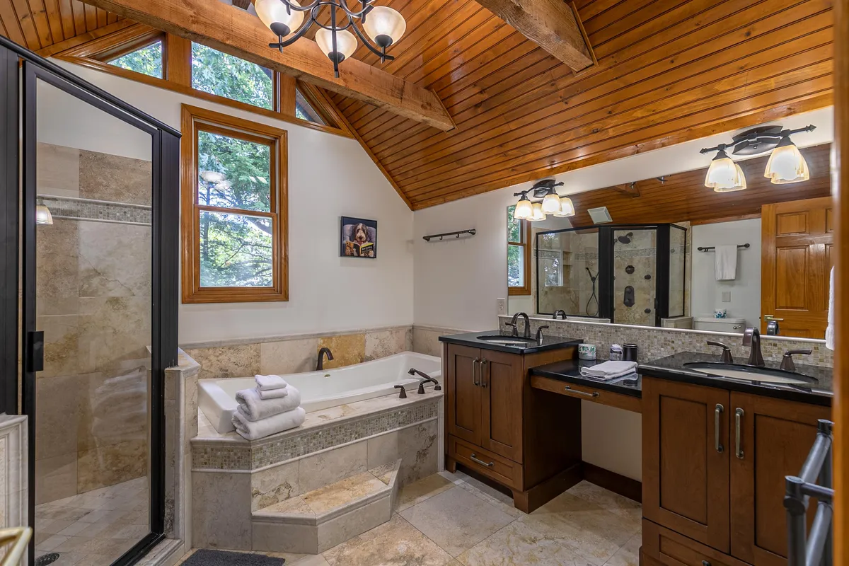A serene, spa-like bathroom featuring a jacuzzi tub, double vanity, shower enclosure, and warm wooden accents. The room is bright, spacious, and designed for relaxation and rejuvenation.