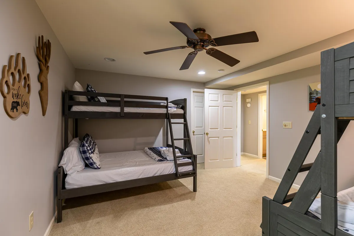 A cheerful bunk room with two sets of bunk beds, wooden wall decor, and a ceiling fan—an inviting haven for sleepovers, games, or cozy movie nights.