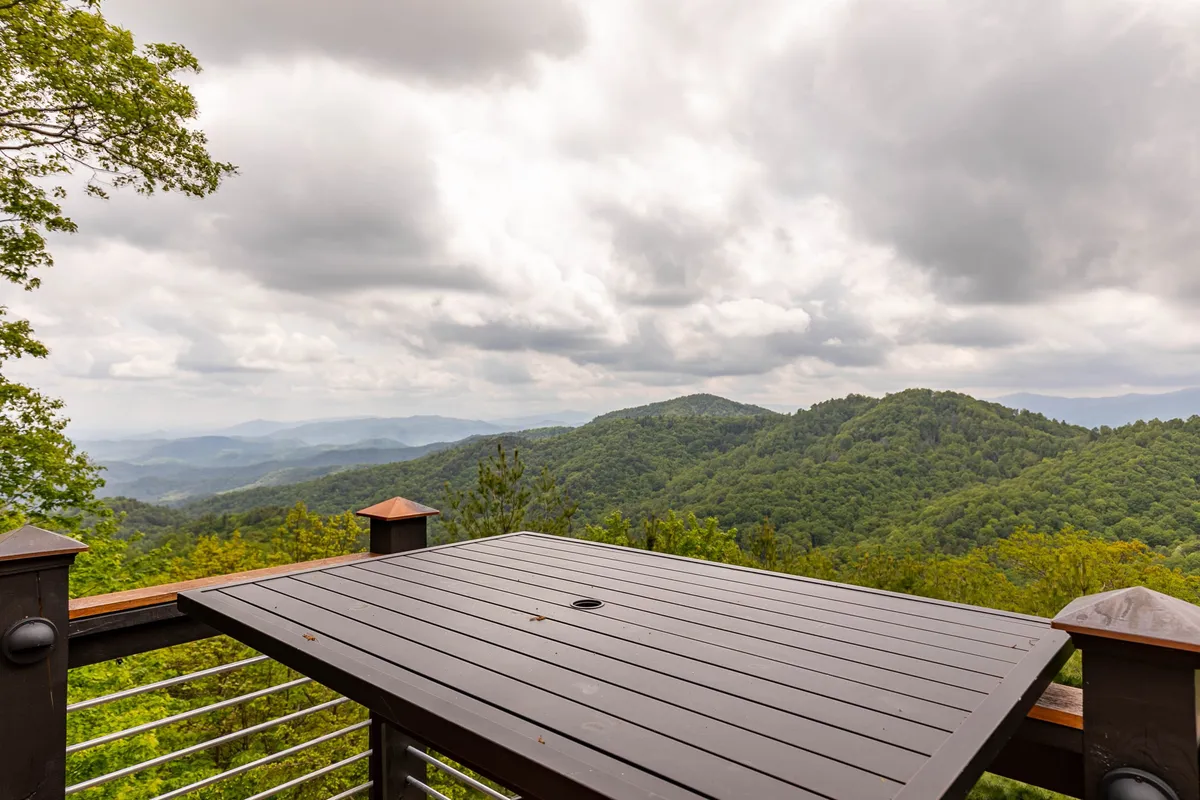 A wide wooden deck facing breathtaking mountain vistas under a dramatic, cloudy sky. The deck seamlessly extends the living space outdoors, inviting guests to relax and appreciate nature's tranquility.