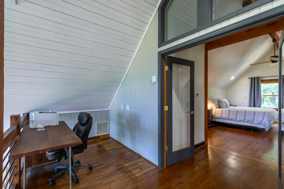 A tranquil bedroom with a comfortable bed, a desk with computer, and a window providing natural light. The setup is both restful and ideal for working remotely, blending relaxation with productivity.