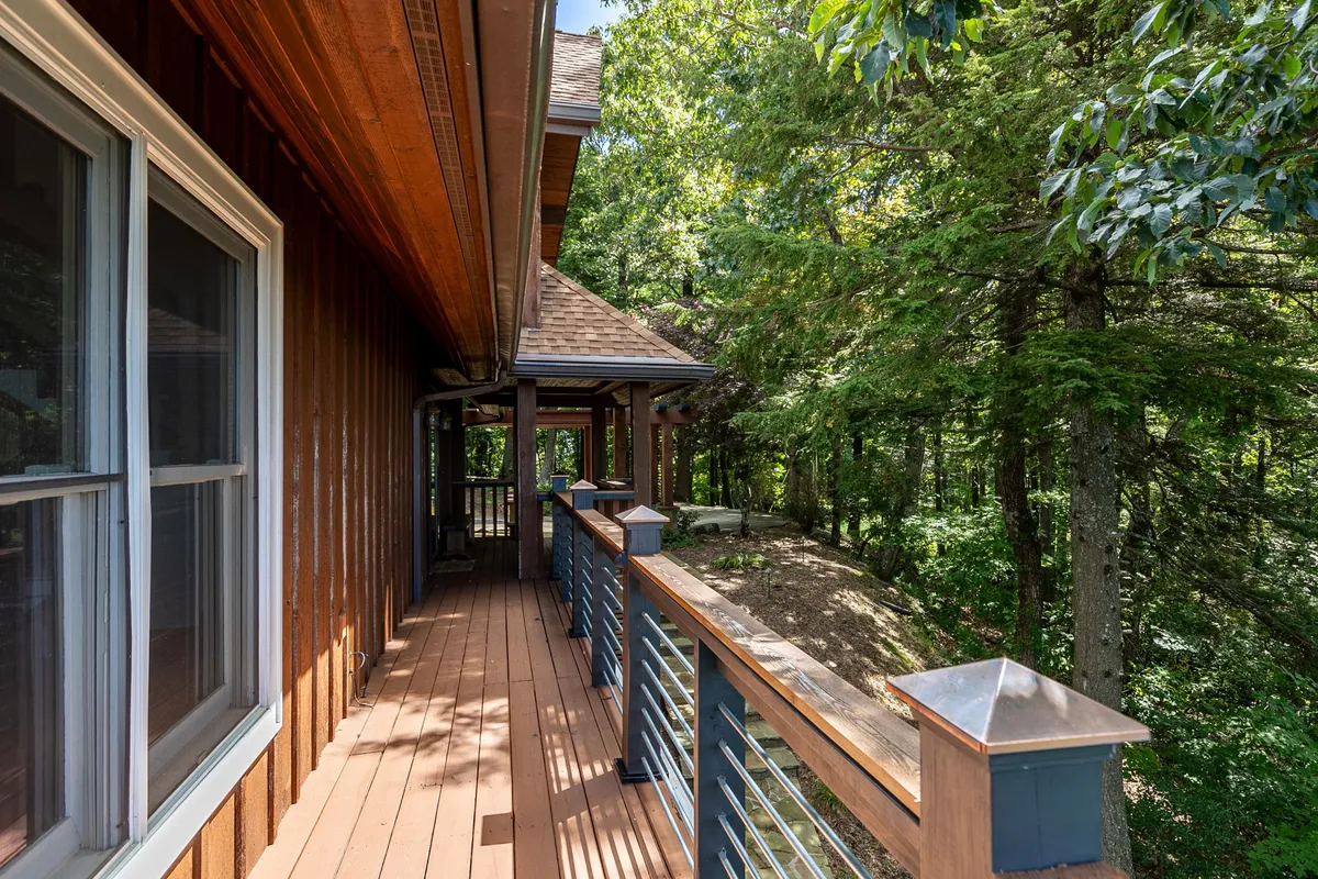 A tranquil wooden deck surrounded by lush trees, featuring a sturdy railing and ample space for outdoor relaxation or gatherings. The vantage point offers glimpses of the forest and hints of mountain views, with the natural landscape creating a sense of seclusion and immersion in nature.