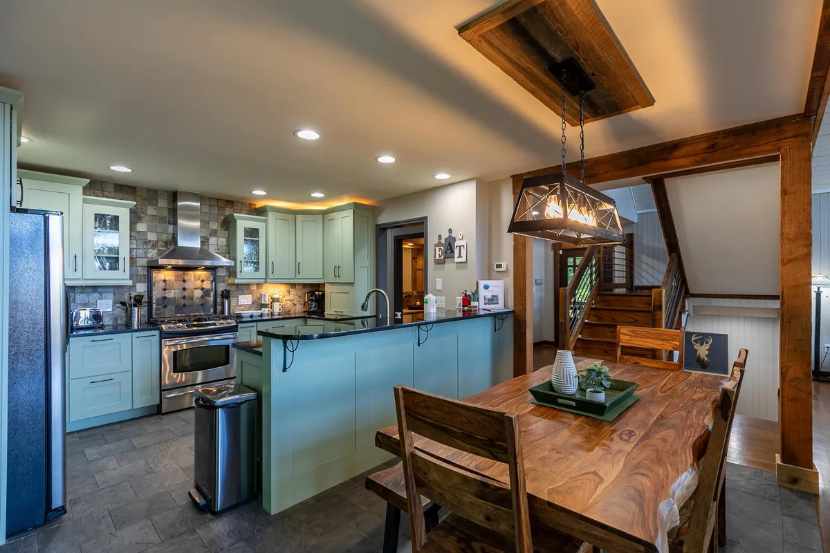 A cozy dining and kitchen area featuring a solid wood table, kitchen island, exposed wooden beams, and warm lighting. The setup invites family gatherings and shared meals, reinforcing the communal aspect of the home.
