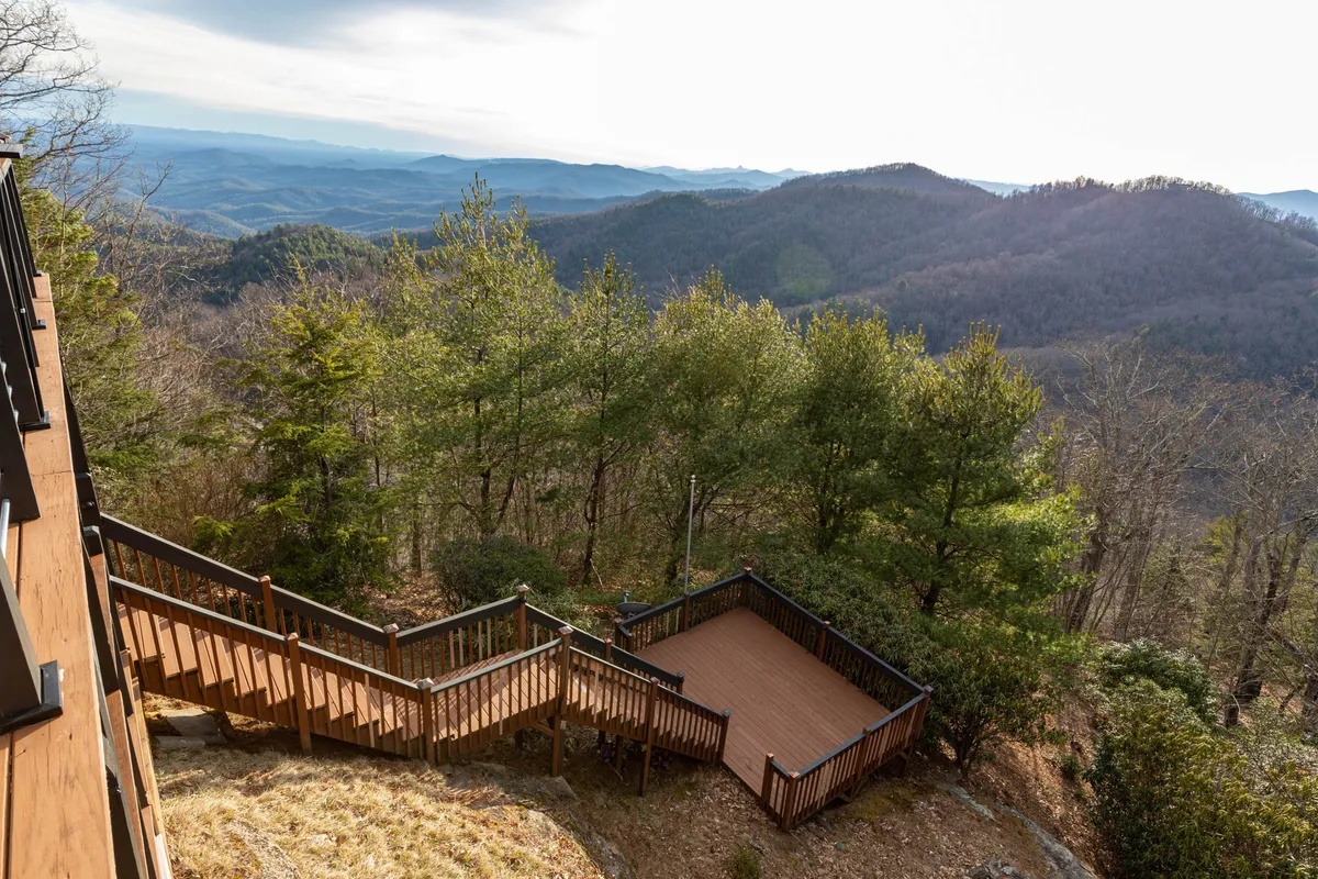 A wooden deck overlooks serene mountain views, surrounded by lush trees. The space invites outdoor gatherings, relaxation, and enjoying nature, with ample seating for family or friends.