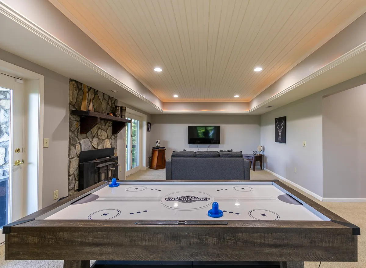 A relaxed entertainment area showcasing an air hockey table, a comfortable sofa, a television, and a fireplace. The layout is ideal for casual hangouts, watching movies, or friendly competition.